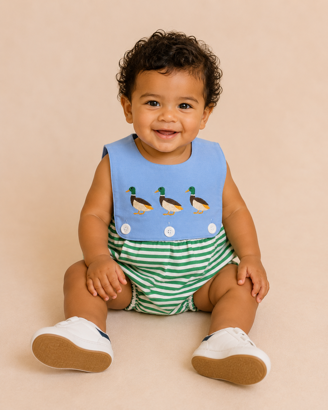 Baby wearing a blue bib with duck designs and green striped shorts on a beige background
