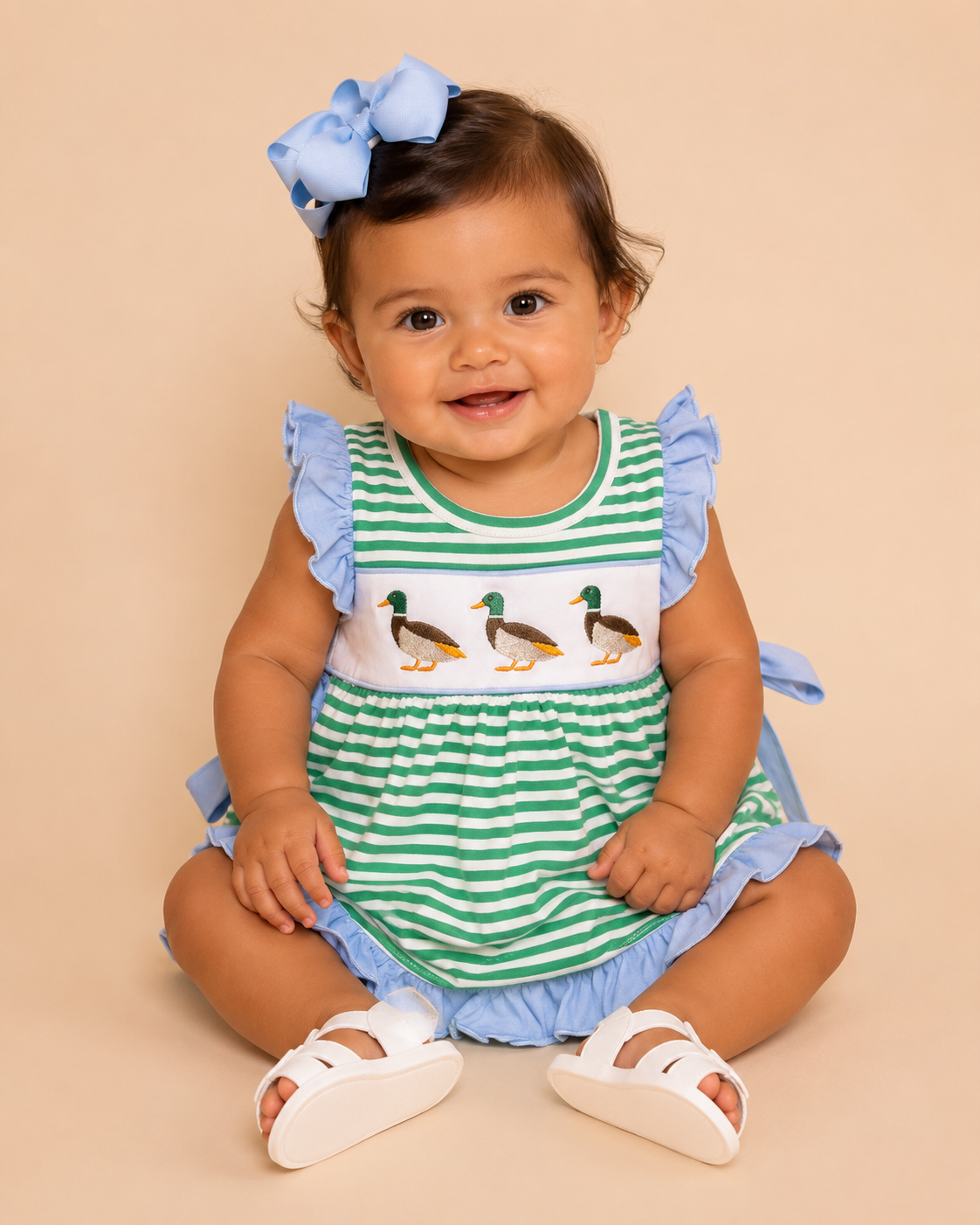 Baby wearing a green and white striped outfit with duck design and blue ruffles on a beige background