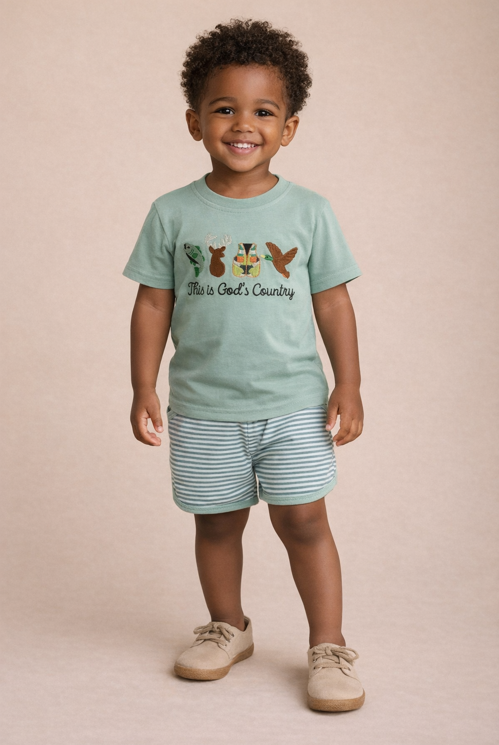 Child wearing a light green t-shirt with a graphic design and text, standing against a beige background.