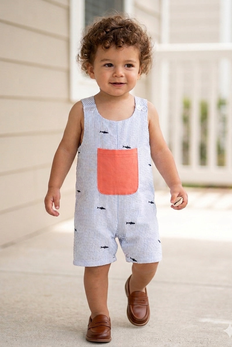 Child wearing a light blue romper with a pink pocket and black fish patterns, standing on a porch.