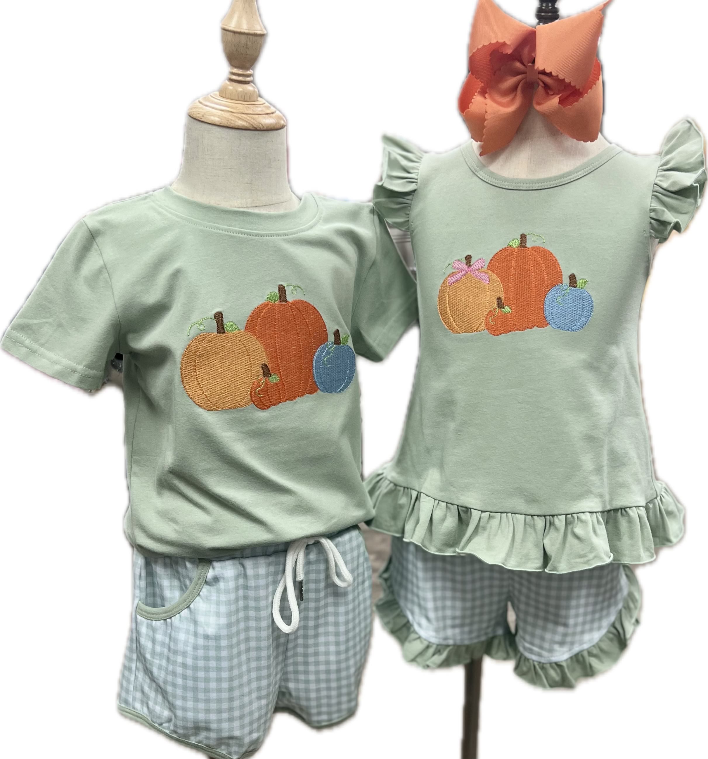 Two children's outfits on mannequins with pumpkins and checkered shorts.
