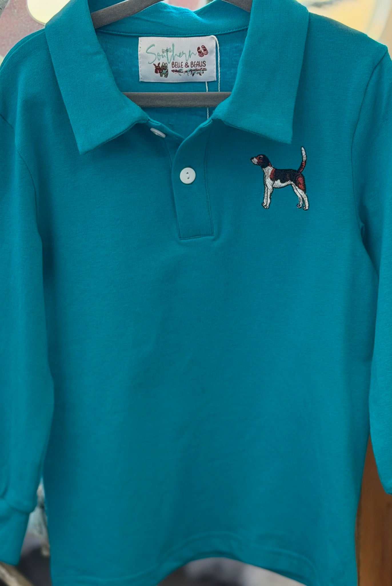 Teal long-sleeve polo shirt with dog embroidery on a hanger