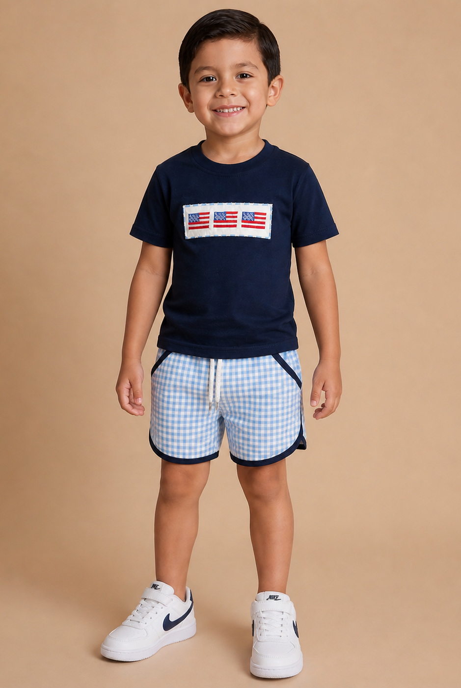 Boy wearing a navy shirt with three flags on the front with gingham shorts.