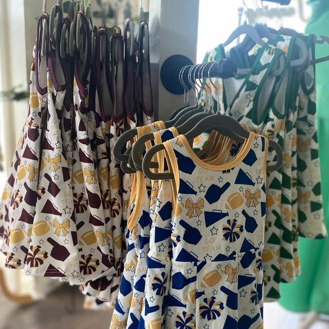 Children's patterned dresses hanging on a rack with wooden hangers.