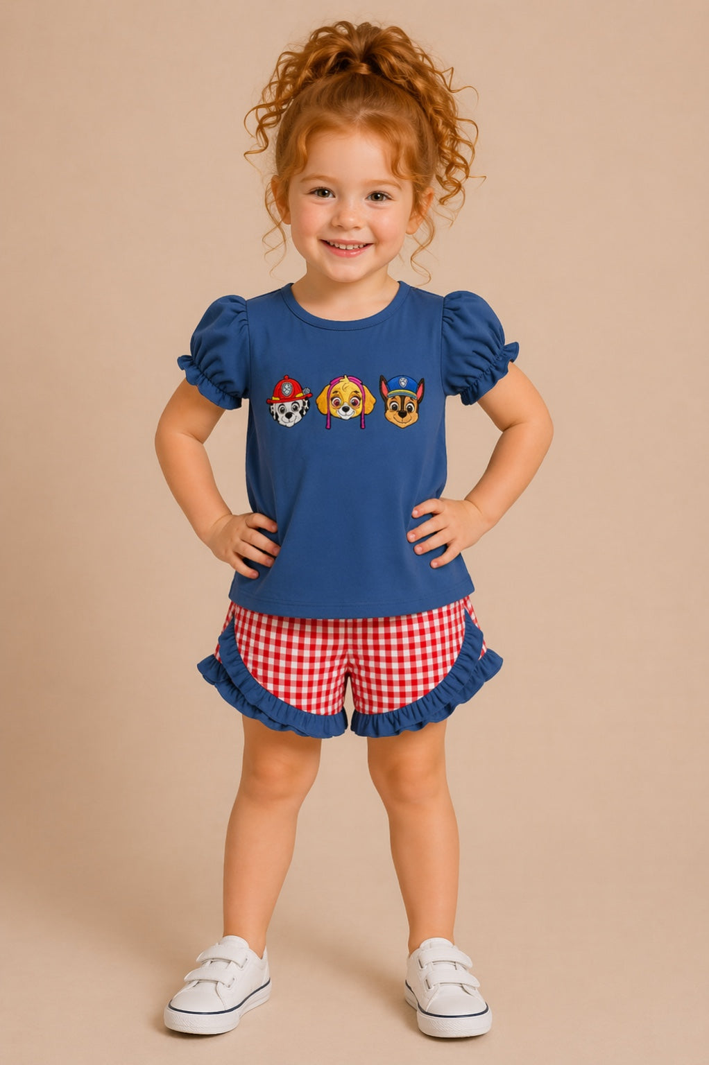 Child wearing a blue top with Paw Patrol graphics and red checkered shorts on a beige background