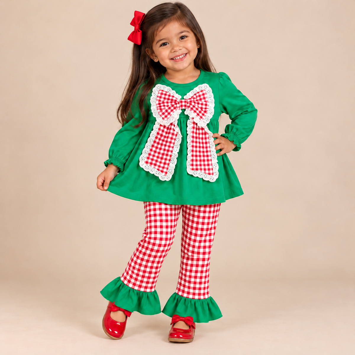 Toddler girl wearing a long sleeve green top with a big red & white gingham bow with matching gingham pants.