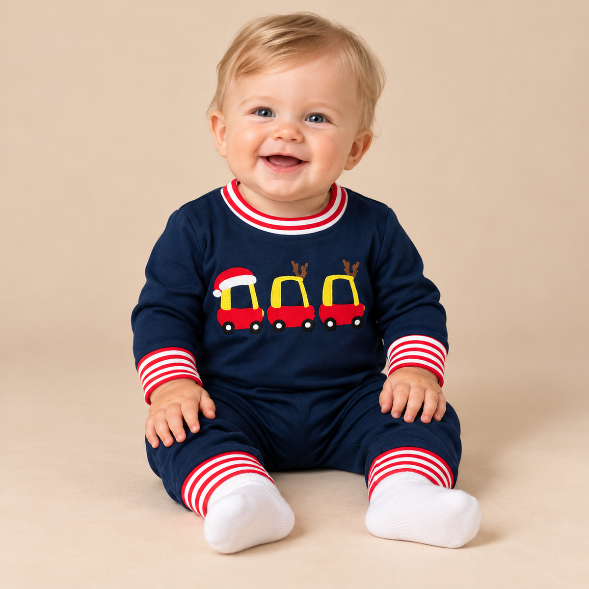 Baby boy model sitting with a navy romper trimmed in red and white stripes.