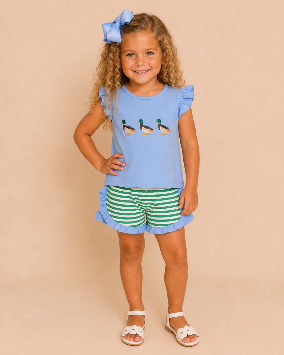 Young girl wearing a blue top with duck designs and green striped shorts on a beige background
