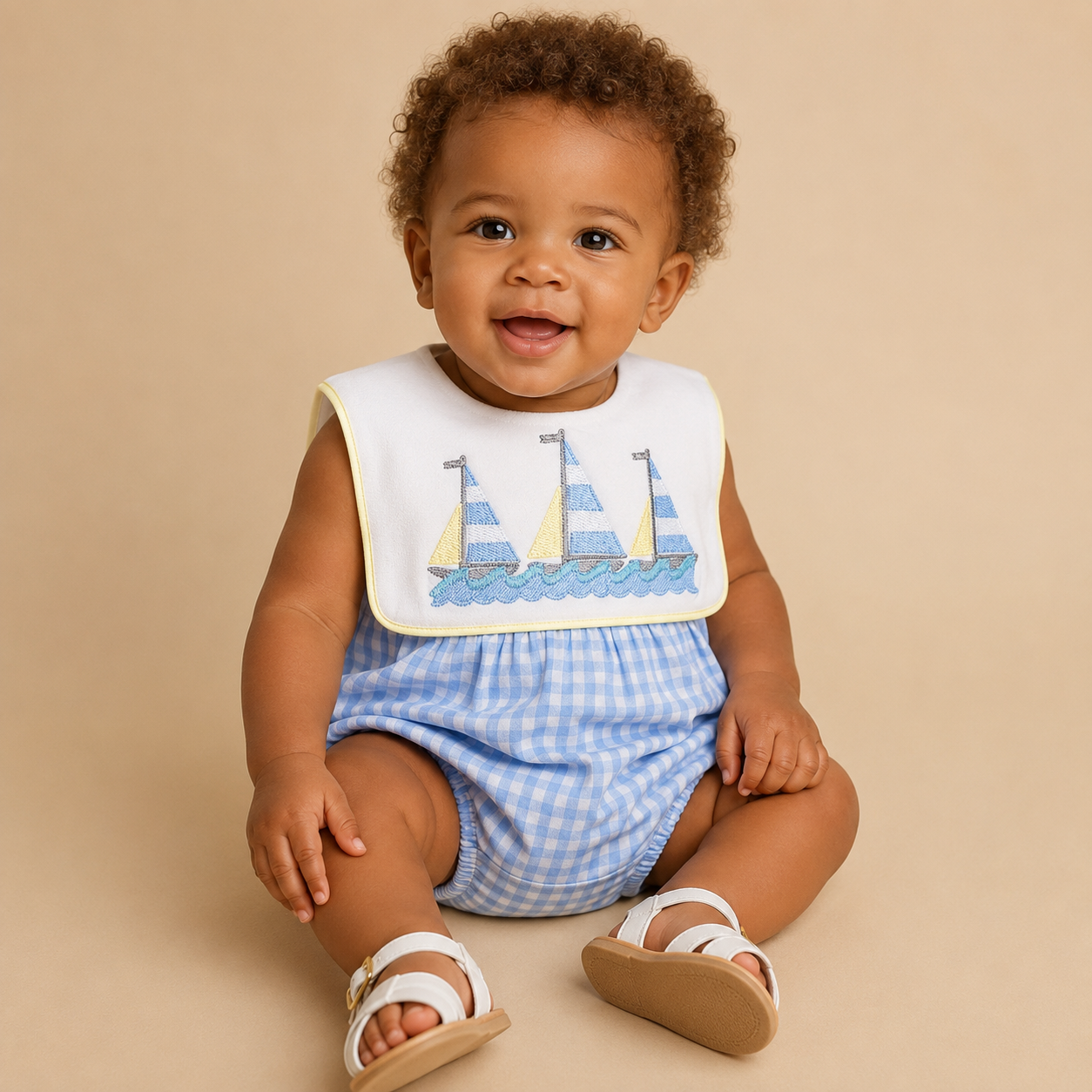 Baby boy wearing a blue gingham bubble with sailboat embroidery.