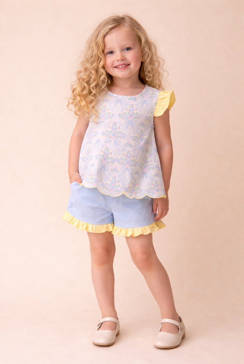 Young girl wearing a white top with yellow trim and light blue shorts on a beige background