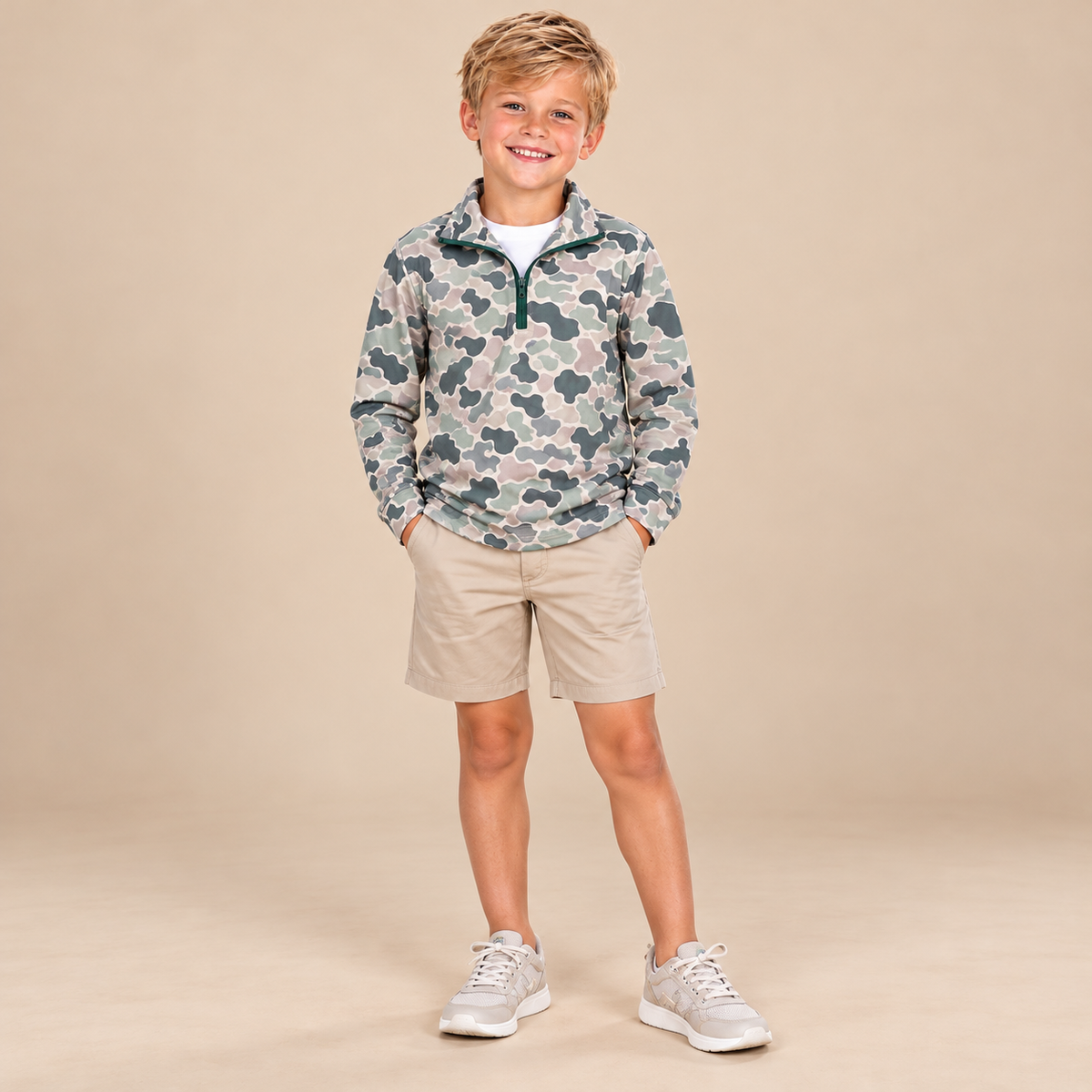 Boy wearing the Marsh Mud long-sleeve athletic camo quarter zip with a stand collar, styled with tan shorts.