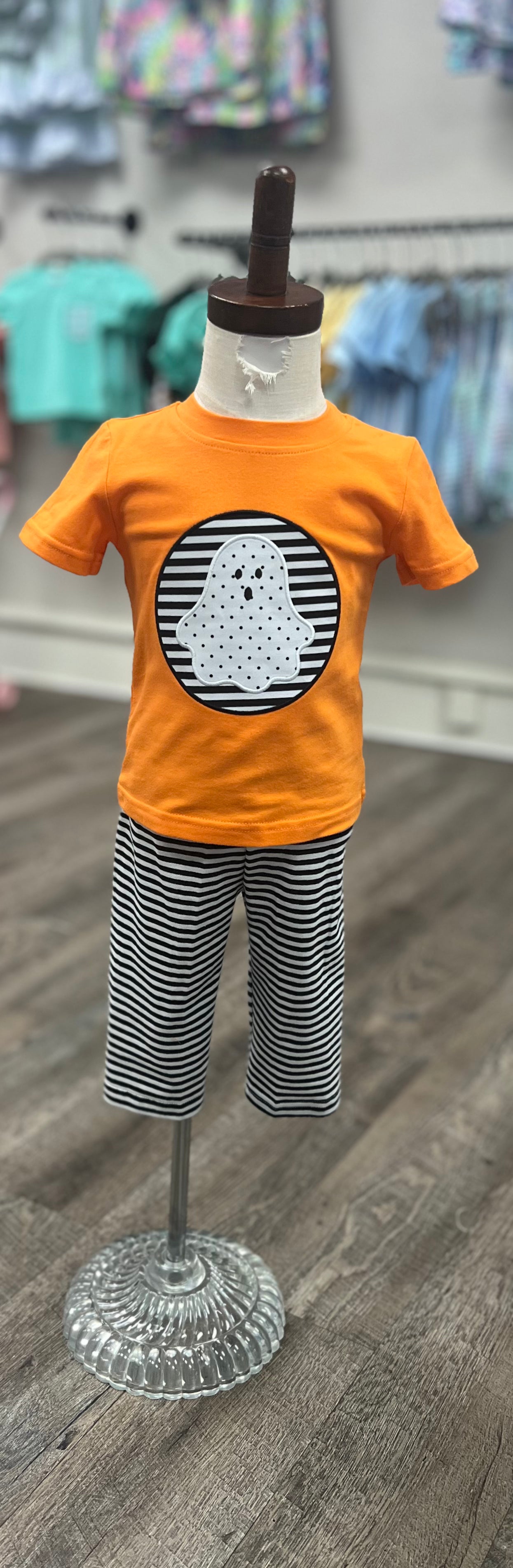 Children's outfit with orange shirt and striped pants on a mannequin against a store background.