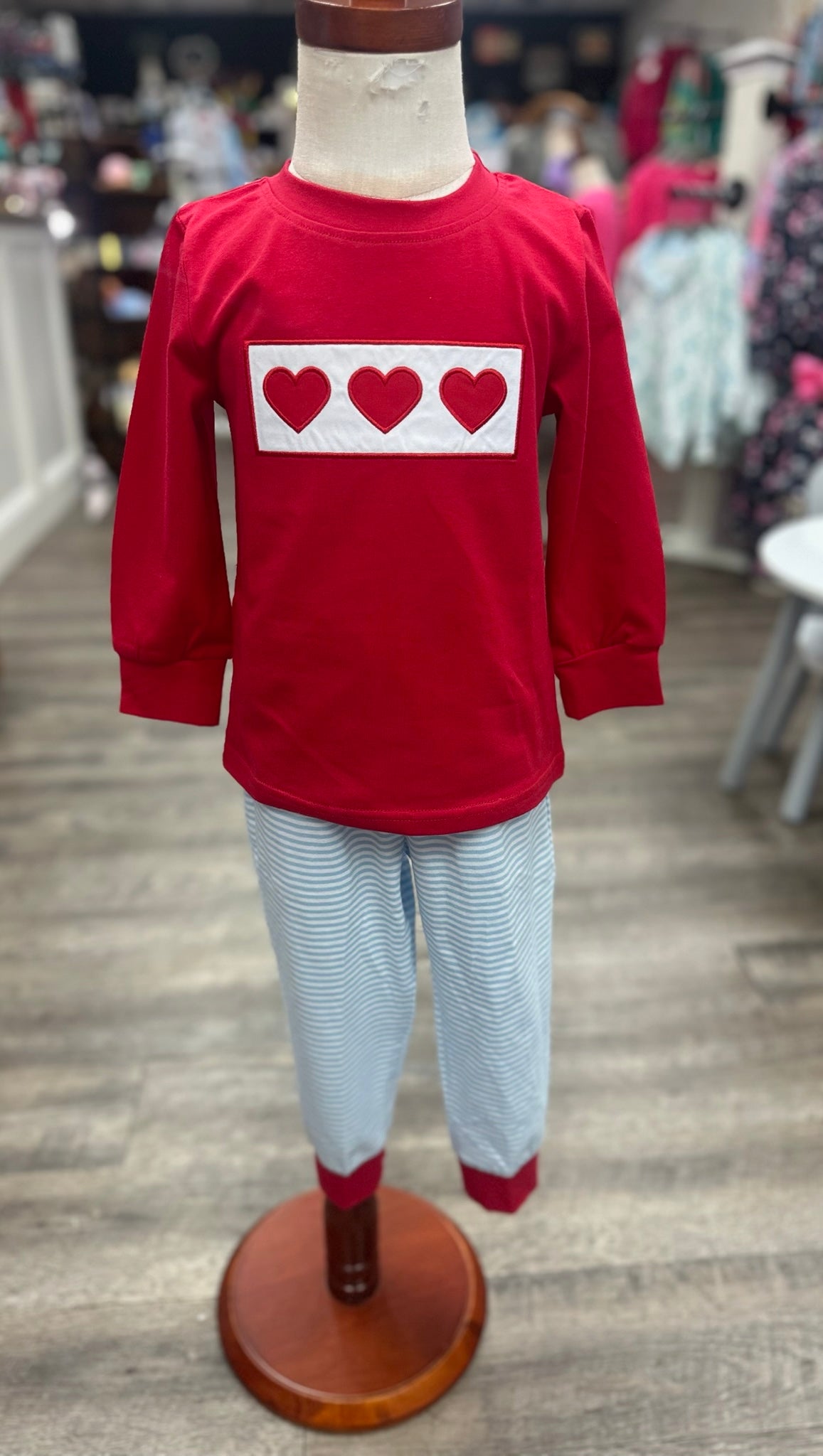 Red long-sleeve shirt with heart design on a mannequin in a store setting.