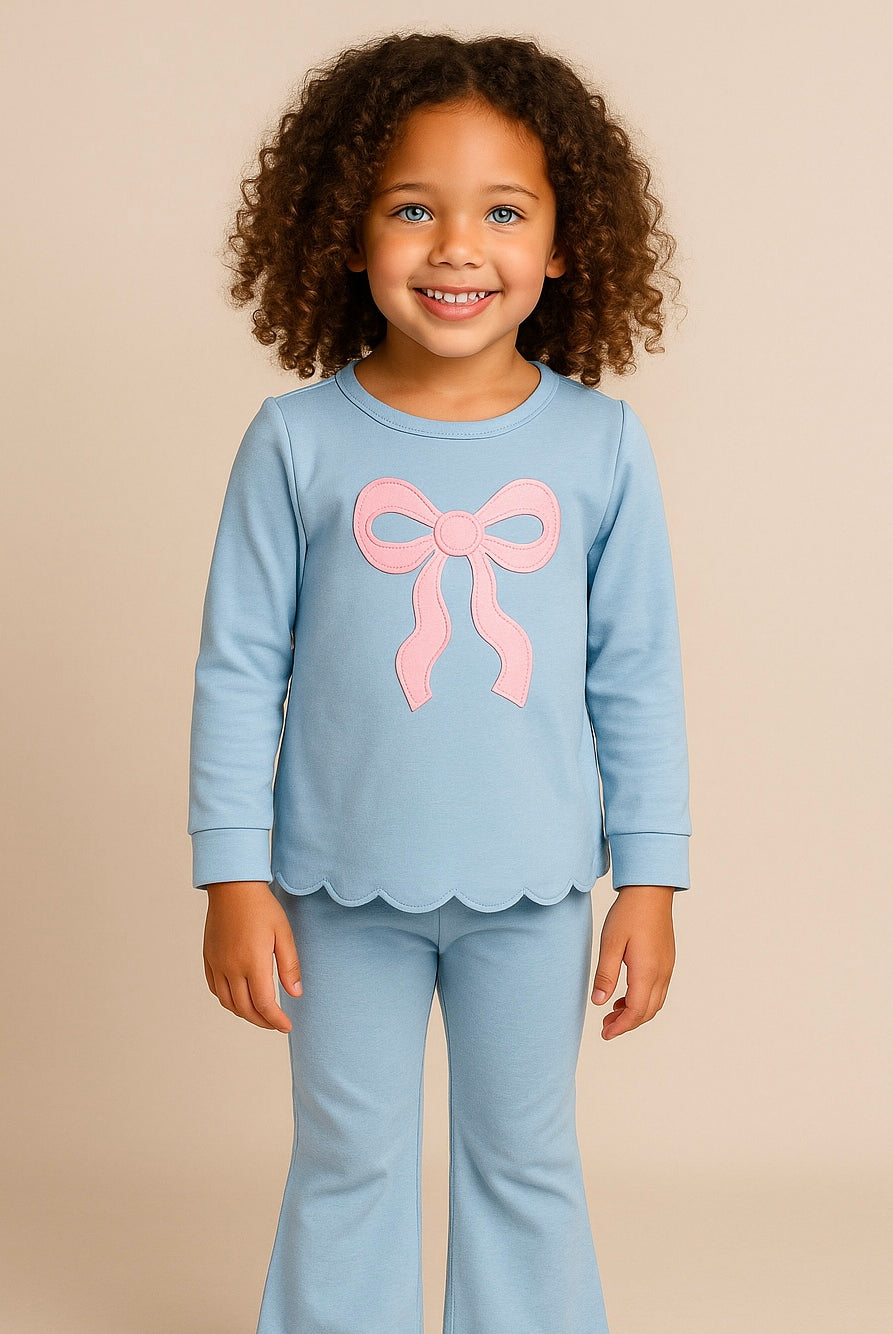 Child wearing a light blue outfit with a pink bow on a beige background