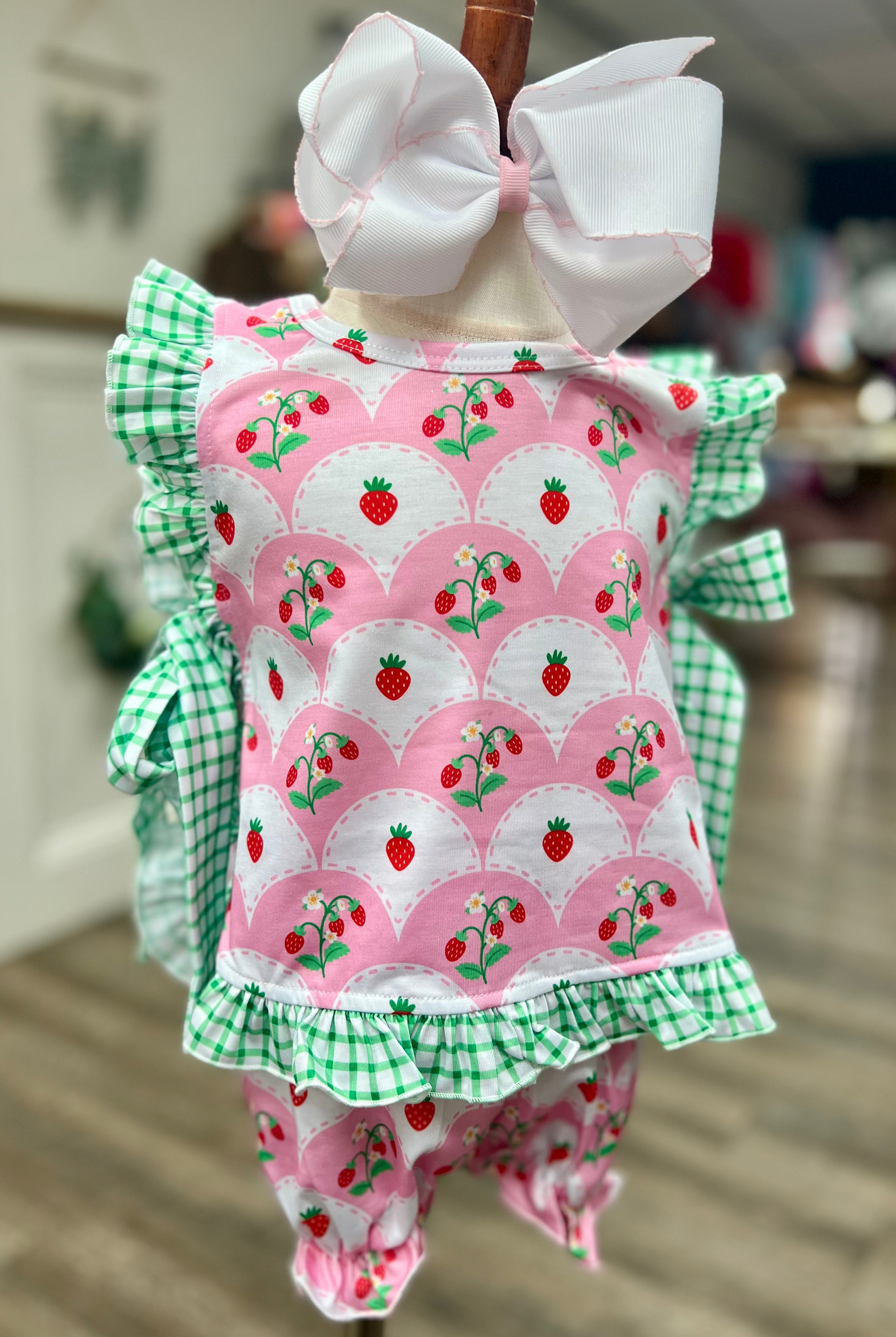 Children's outfit with pink strawberry pattern and green checkered details on a mannequin.