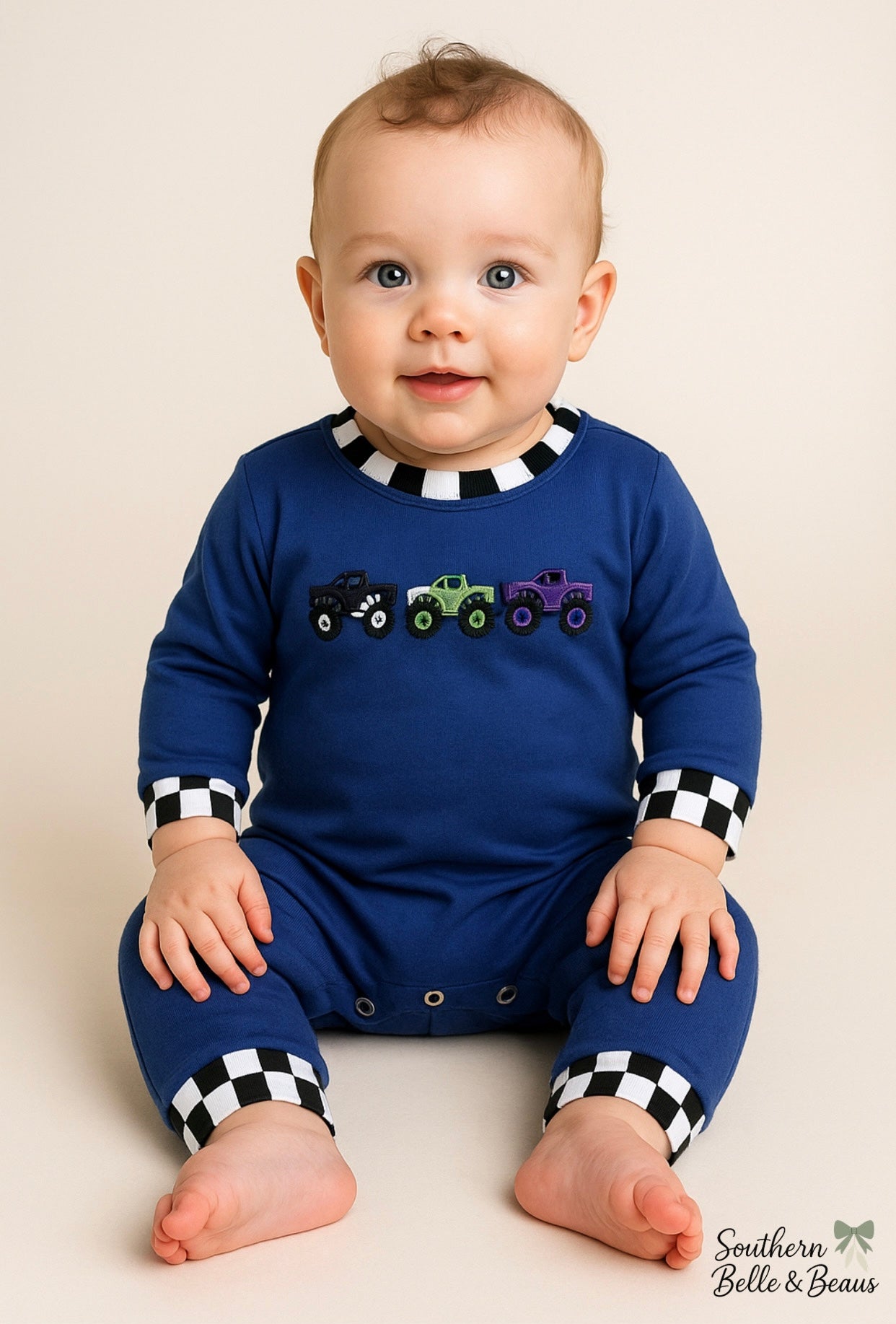 Royal blue baby boy romper with monster truck appliqués and black-and-white checkered trim.