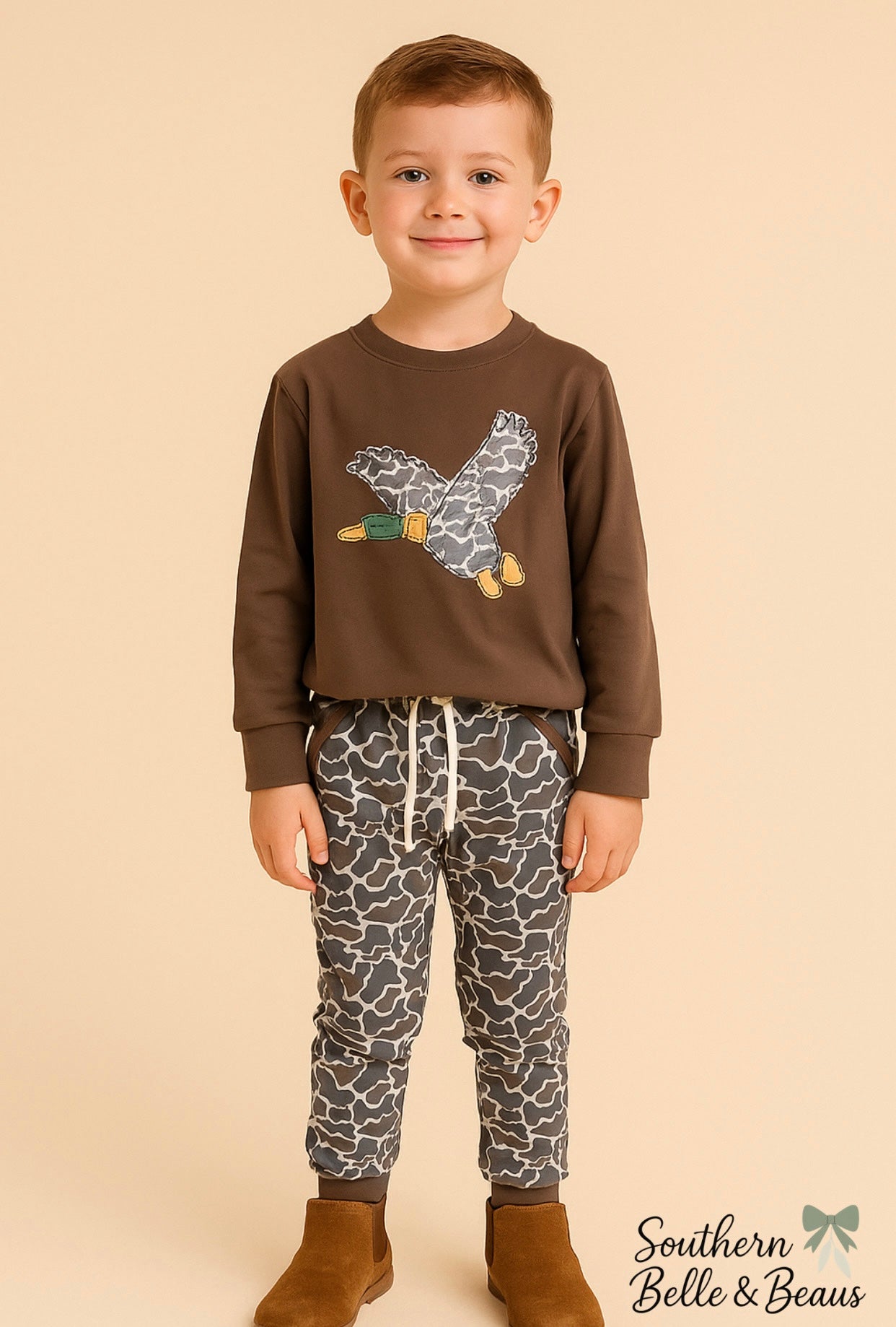 Boy wearing a brown shirt with a duck design and camo joggers.