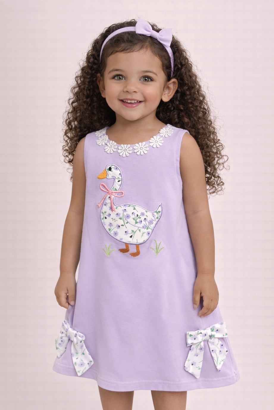 Young girl wearing a purple dress with a floral duck design on a light pink background