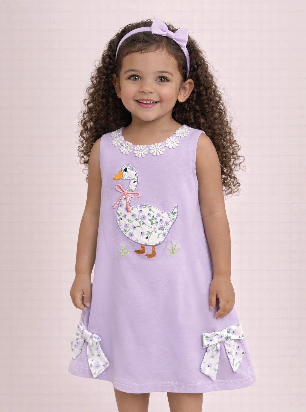 Young girl wearing a purple dress with a floral duck design on a light pink background