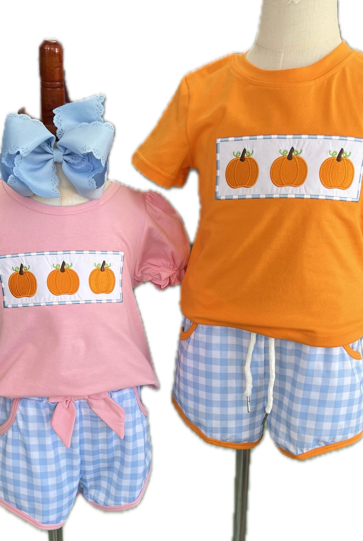 Two children's outfits on mannequins with pumpkin design shirts and checkered shorts.