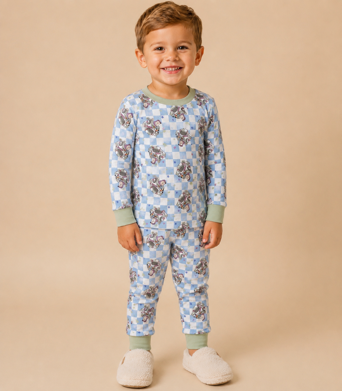 A young child wearing a light blue and white checkered long-sleeve pajama set with astronaut print , standing against a solid beige background.