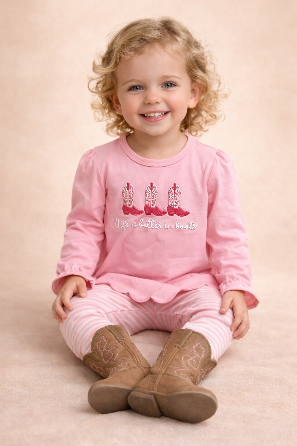 Little blonde girl wearing a pink jogger set with boots on the front.