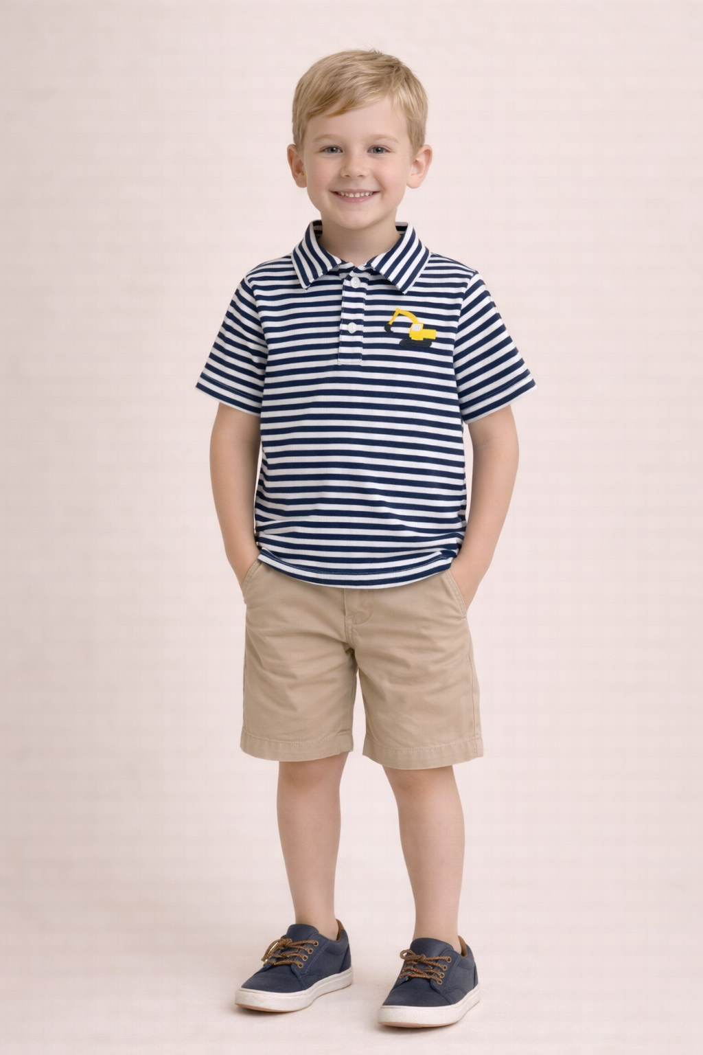 Young boy wearing a striped polo shirt and shorts on a light pink background