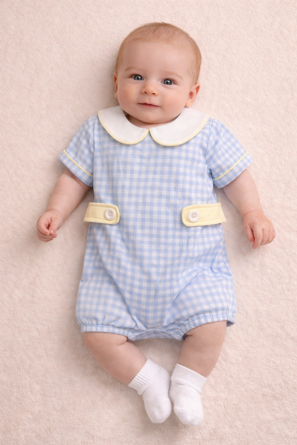 Baby boy wearing a light blue gingham bubble with yellow accents.