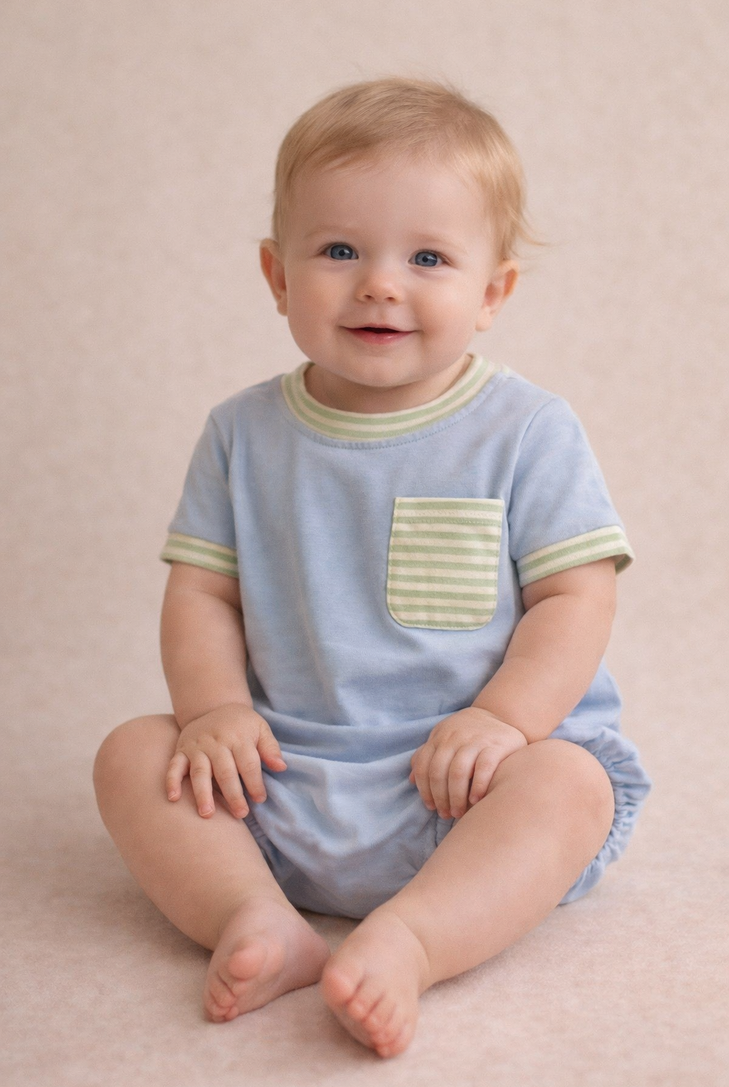 Baby wearing a light blue romper with green trim on a beige background