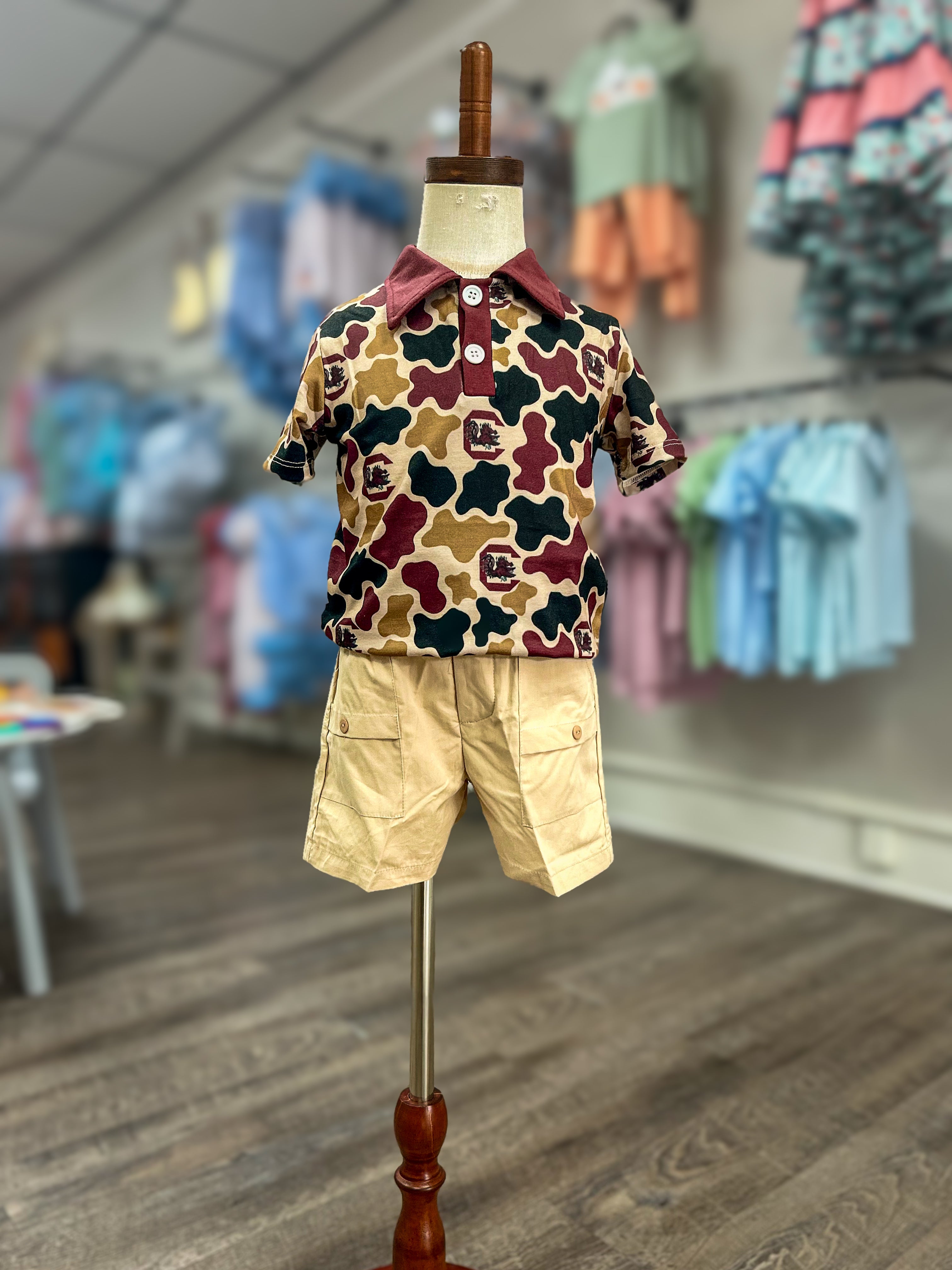 Children's outfit with camouflage shirt and beige shorts on a mannequin in a store setting.