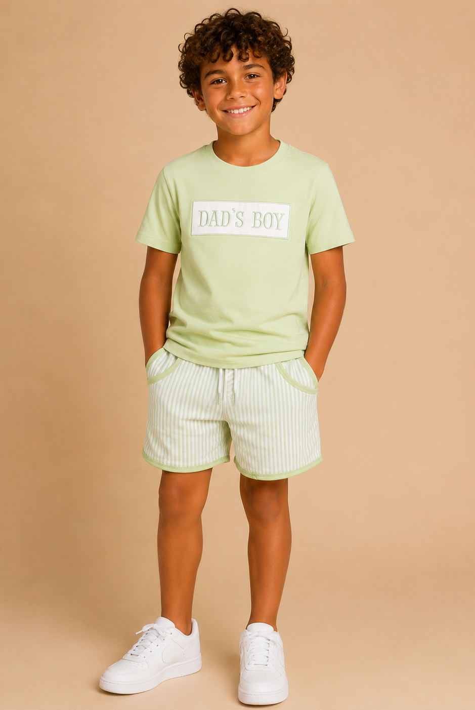Child wearing a light green t-shirt with 'DAD'S BOY' text and matching shorts on a beige background