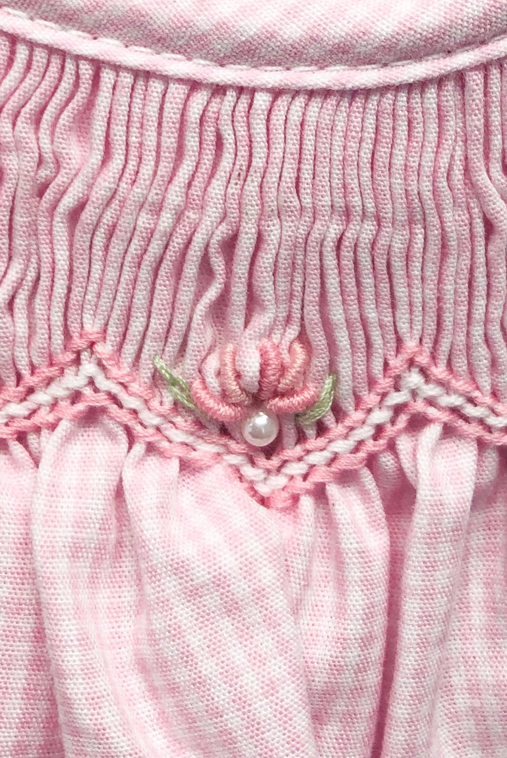 Close-up of a pink textured fabric with floral embroidery and pearl embellishments.