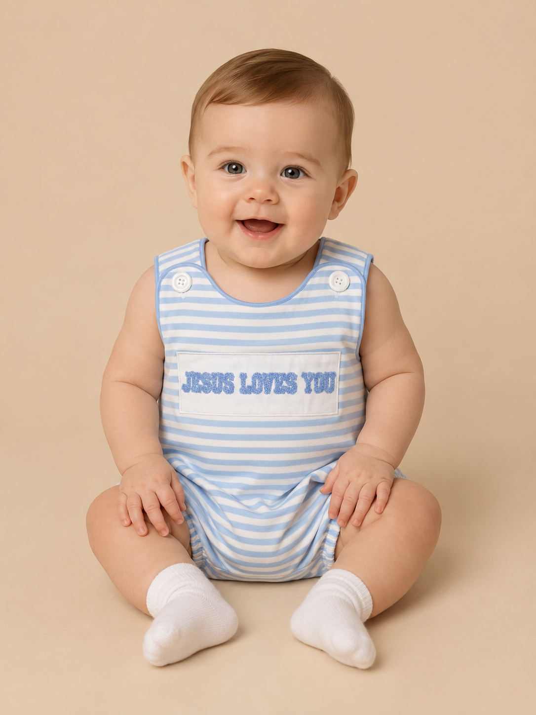 A baby sitting on a beige studio background wearing a light blue and white striped sleeveless romper with the text 'JESUS LOVES YOU' printed on the chest, along with white socks.