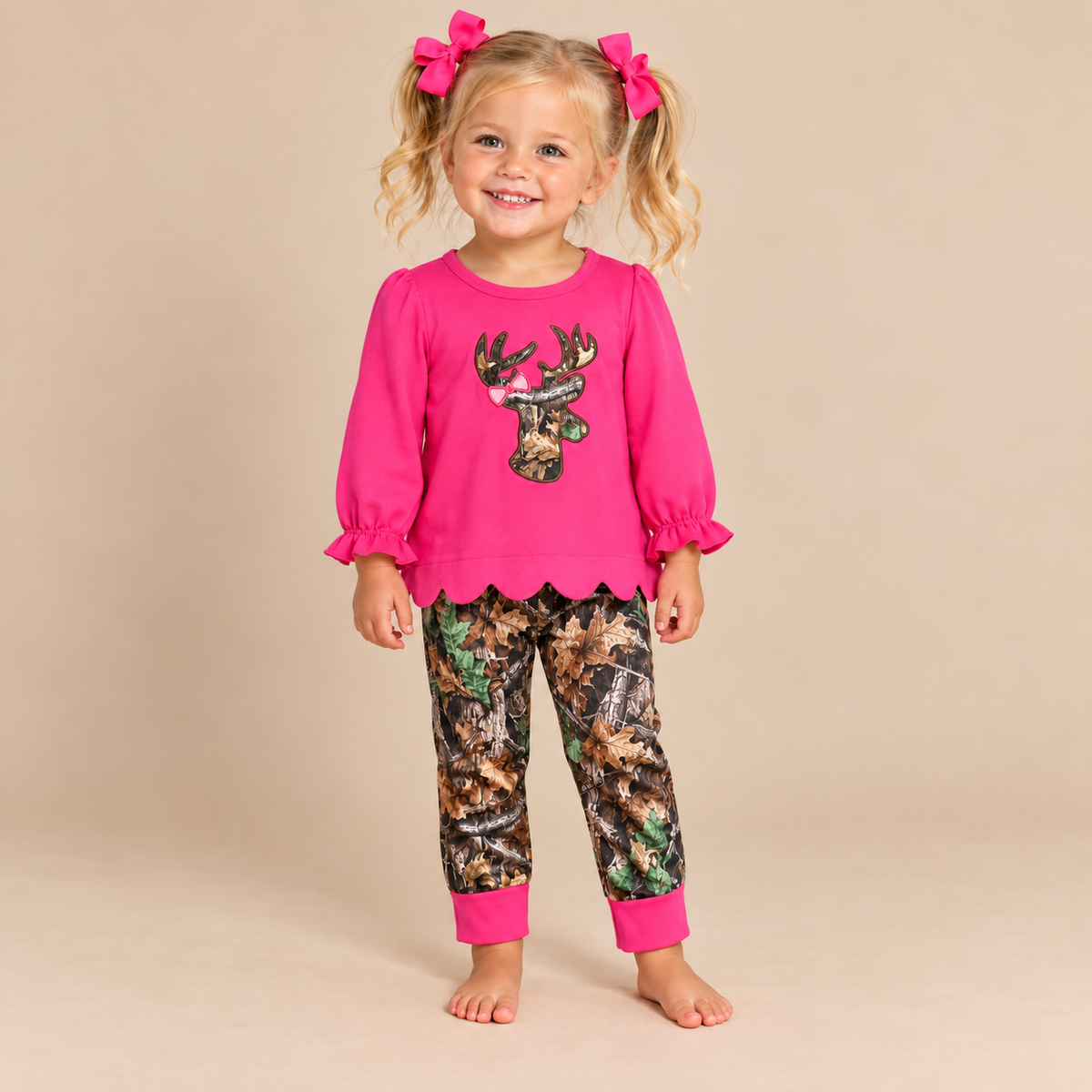 Toddler girl wearing a long sleeve, hot pink shirt with a camo deer embroidered, scalloped hem and camo pants.