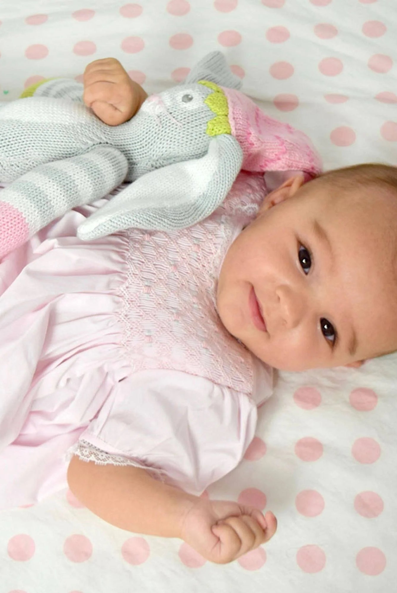 Baby lying on a pink polka dot blanket with a soft toy