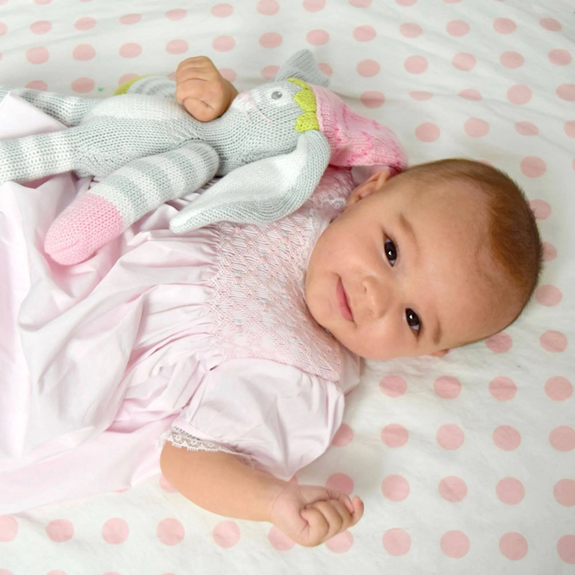 Baby lying on a pink polka dot blanket with a soft toy