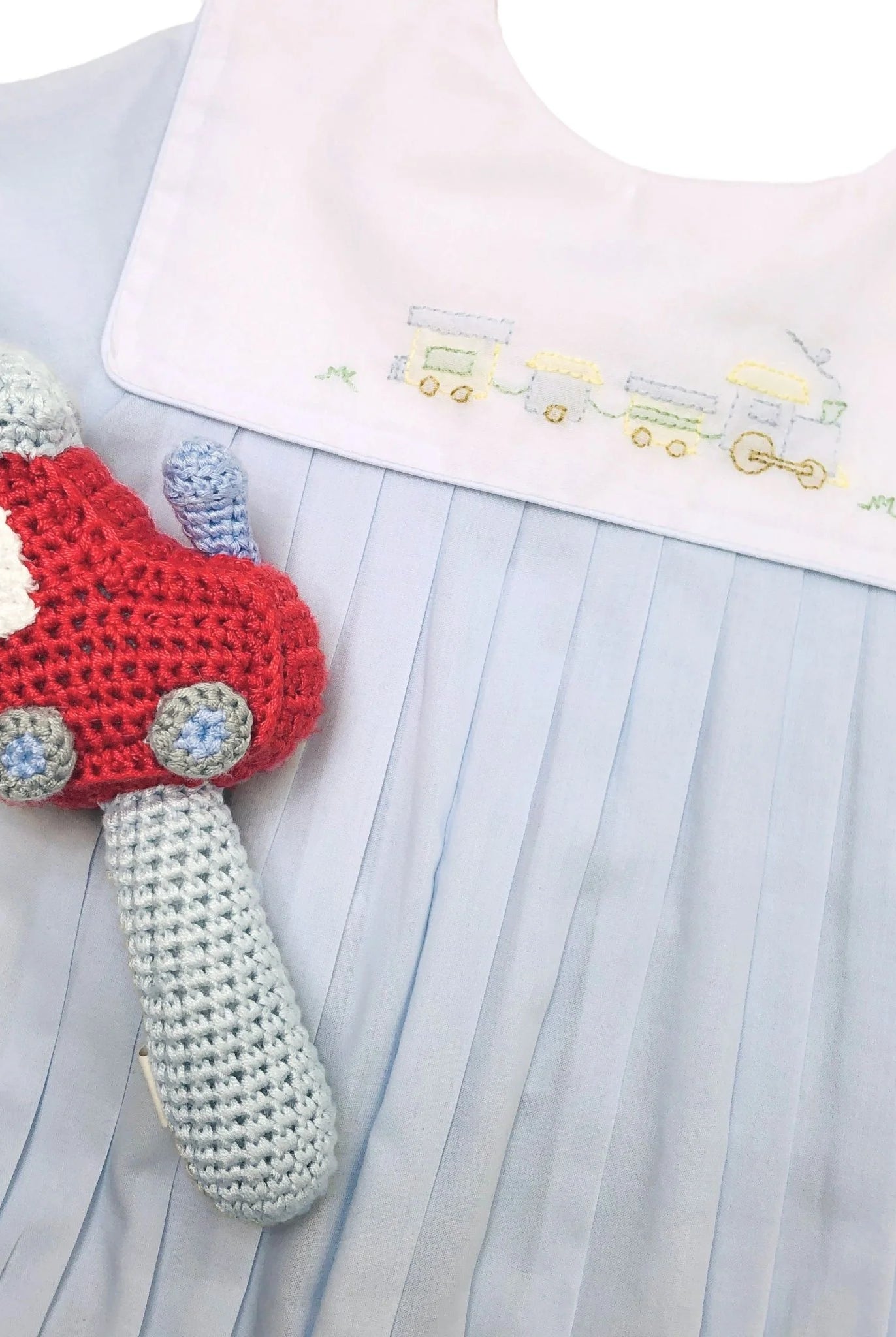 Crocheted toy car held by a child wearing a light blue dress with embroidered details.