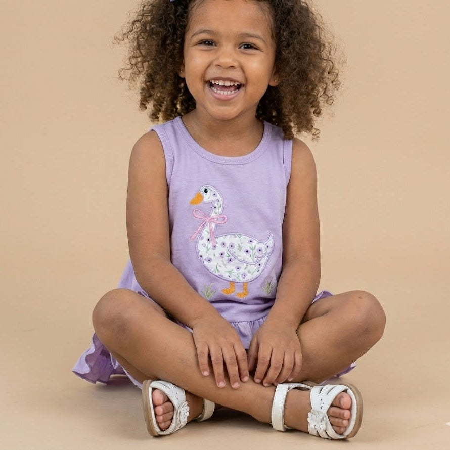 Child wearing a purple sleeveless top with a duck design on a beige background