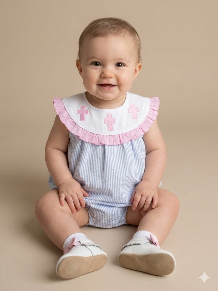 Baby wearing a light blue dress with pink ruffled collar and cross details on a beige background