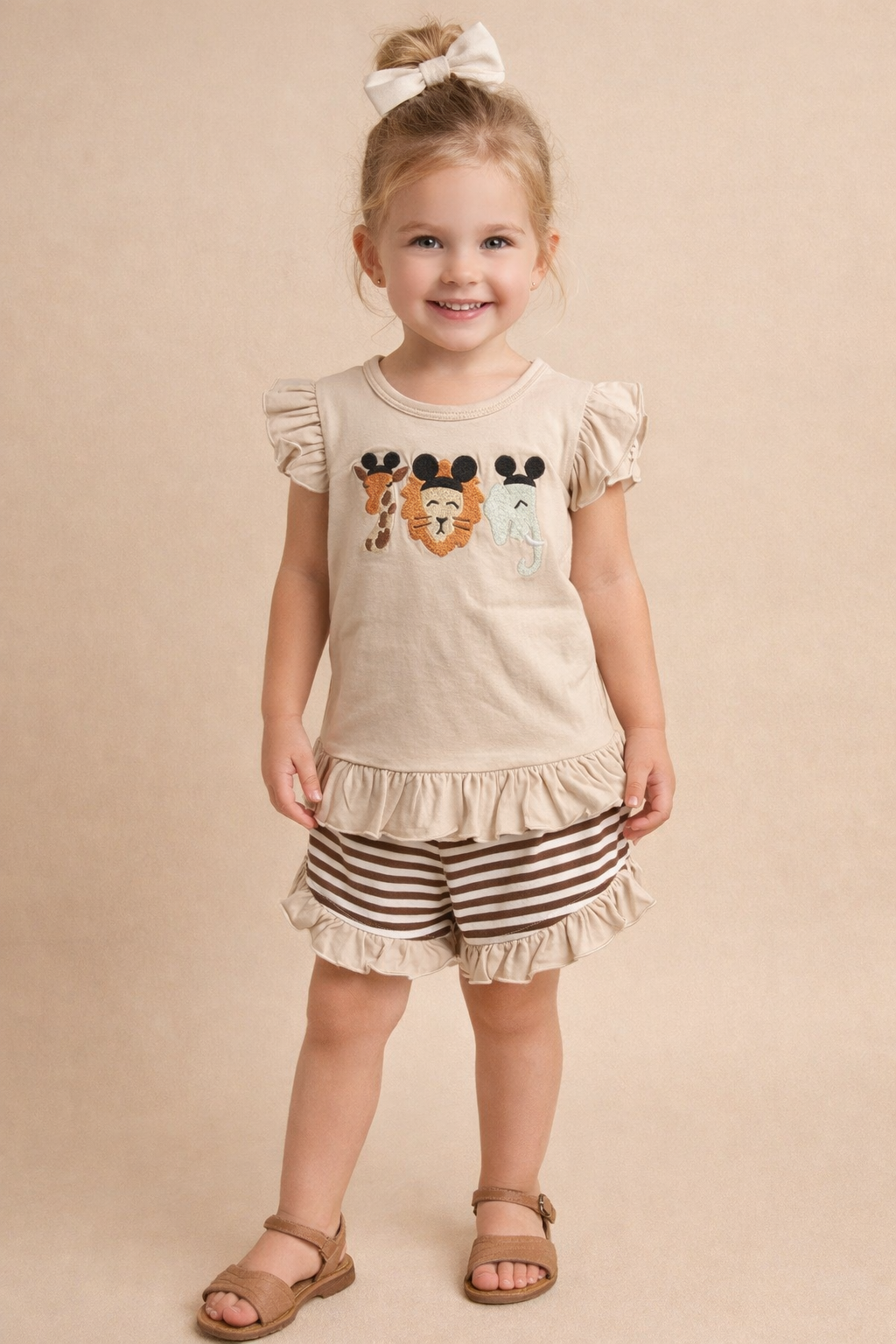 Young girl wearing a beige top with character designs and striped shorts on a beige background