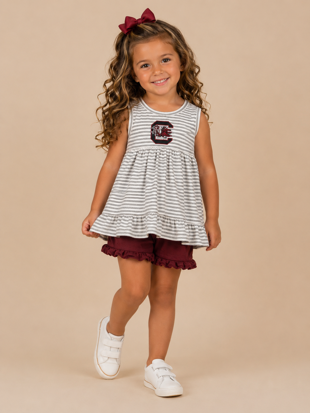 Young girl wearing a striped dress with a logo and maroon shorts on a beige background