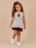 Young girl wearing a striped dress with a logo and maroon shorts on a beige background