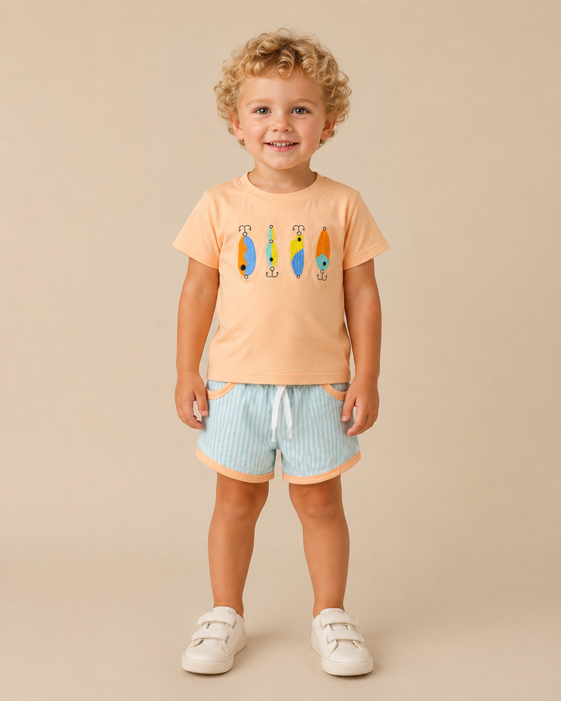 Toddler boy wearing a peach colored shirt with fishing lures embroidered on the front and mint striped shorts.