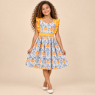 Young girl wearing a pumpkin print dress with orange ruffle accent.