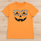 Orange short-sleeve tee with a black jack-o’-lantern face wearing black-and-white polka-dot glasses