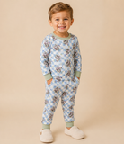 A smiling young boy wearing a light blue and white checkered long-sleeve pajama set with a cartoon dog print, standing against a solid beige background.