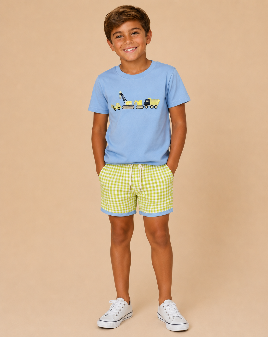 Young boy wearing a light blue shirt with construction embroidery on beige background.