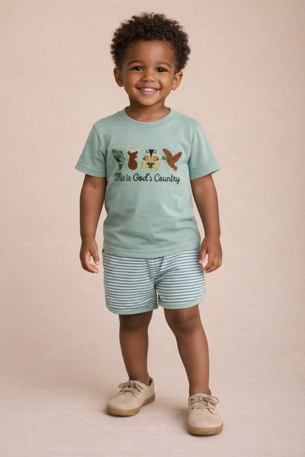 Child wearing a light green t-shirt with a graphic design and text, standing against a beige background.