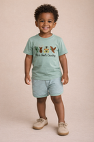 Child wearing a light green t-shirt with a graphic design and text, standing against a beige background.