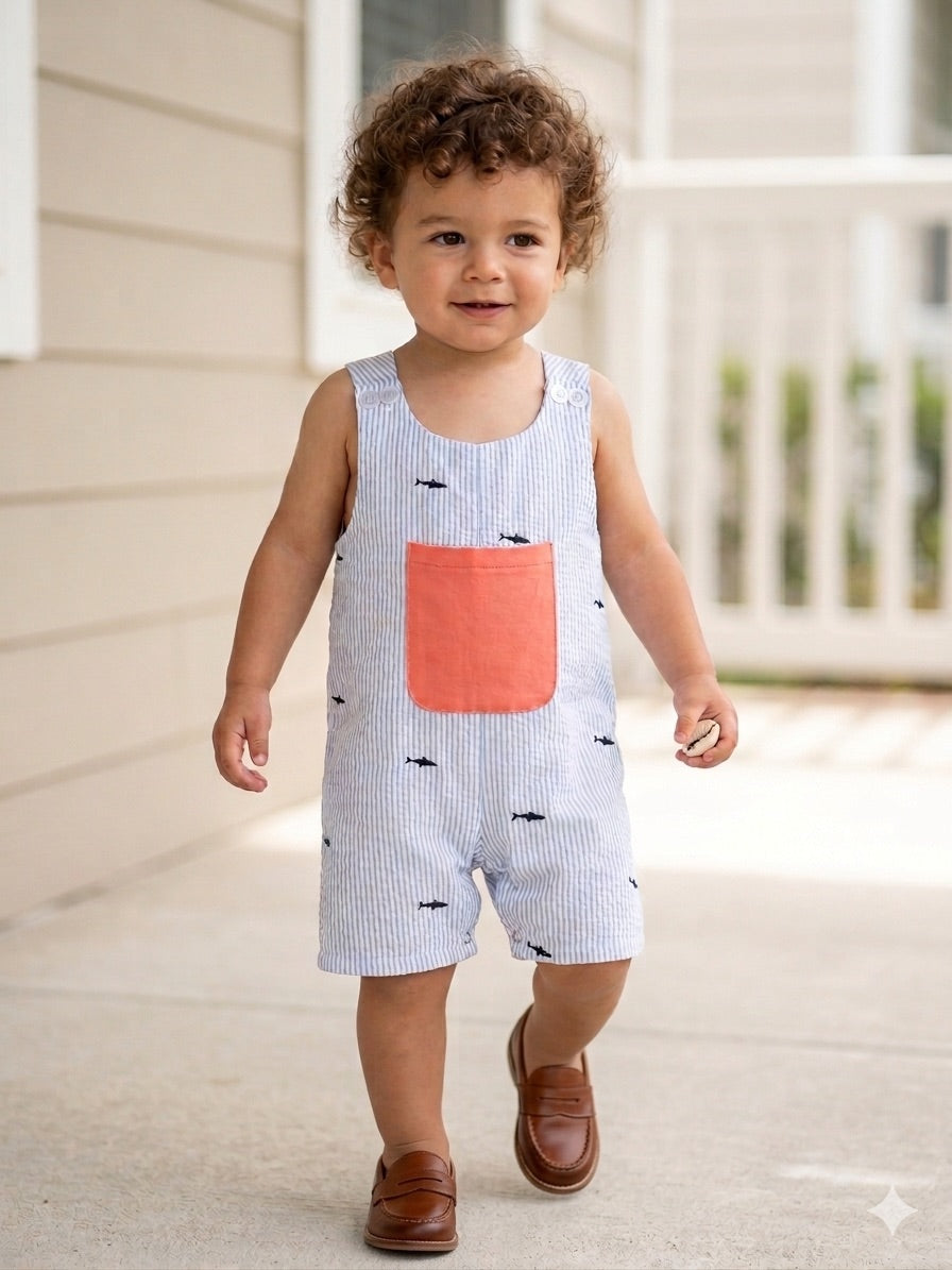 Child wearing a light blue romper with a pink pocket and black fish patterns, standing on a porch.